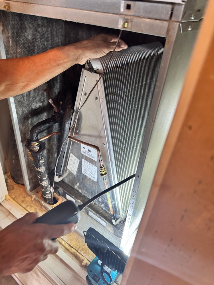 Technician's hands inspecting an evaporator coil inside an air handler